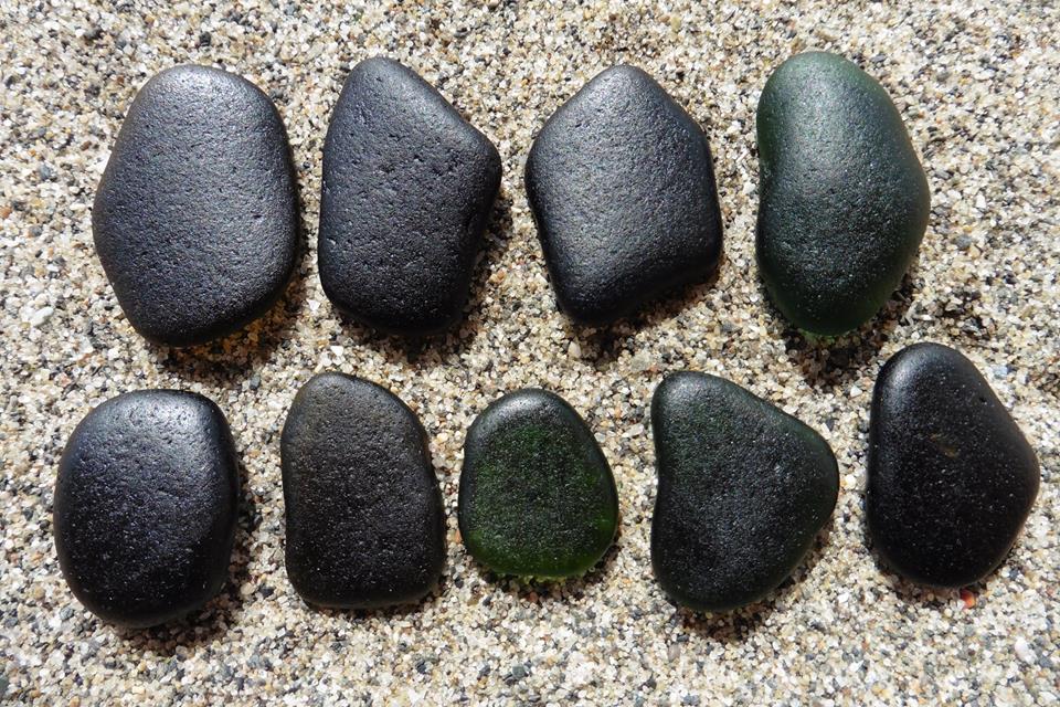 nine pieces of black sea glass lined up in the sand